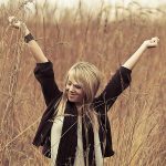 Junge Frau steht in einem Weizenfeld und reckt die Arme in die Höhe